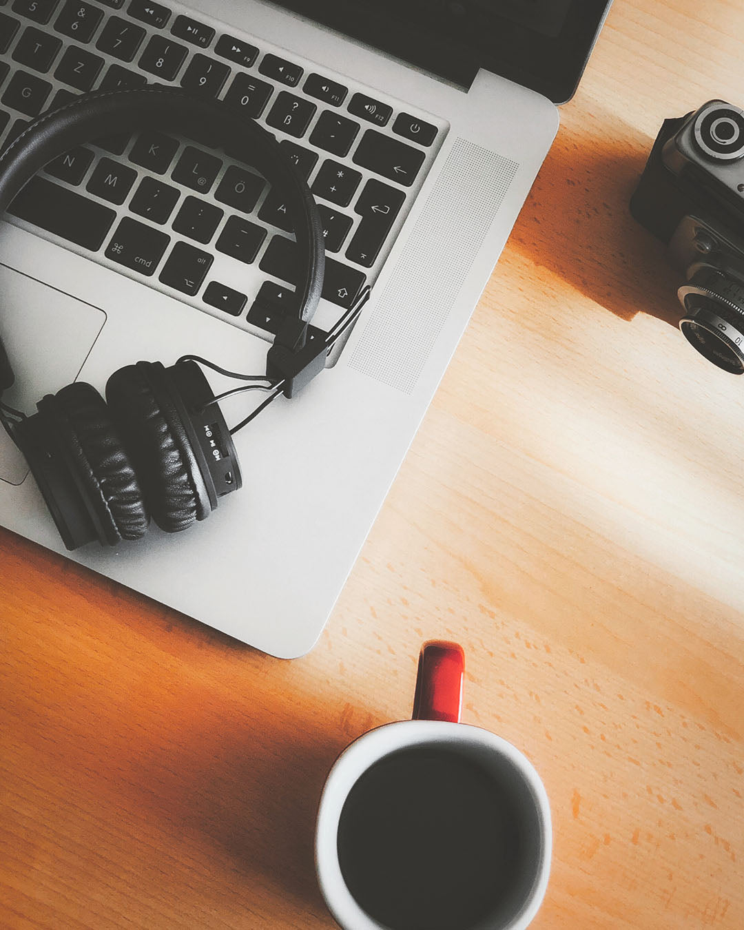 Laptop with headphones, camera, and coffee cup on a wooden desk