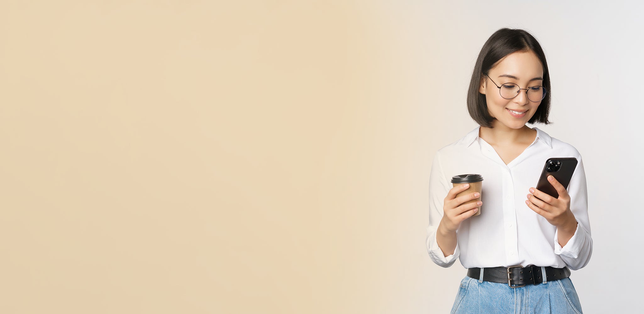 Woman holding a phone and a cup against a beige background