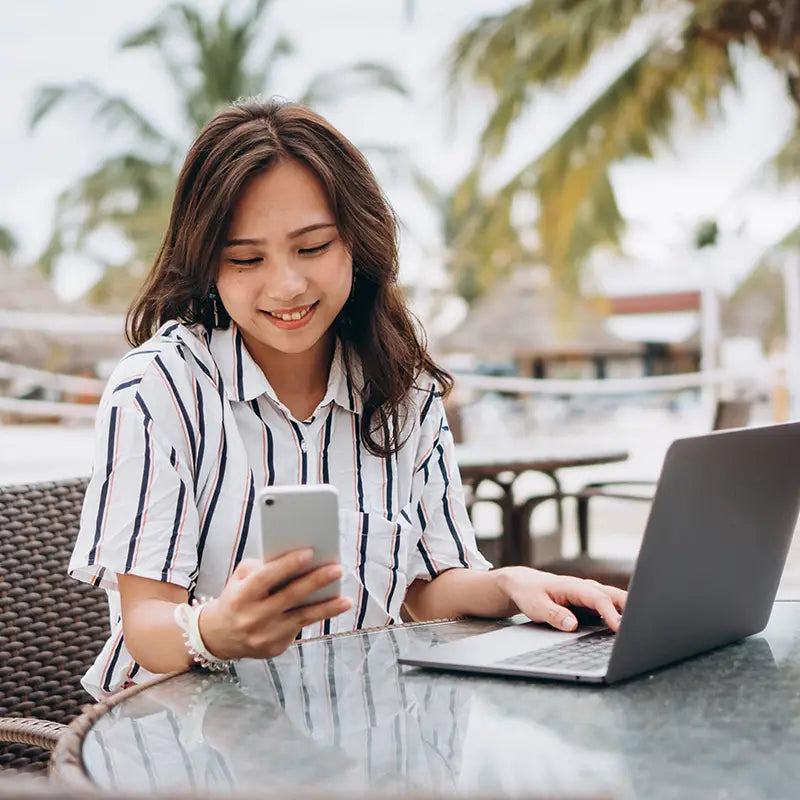Woman using a laptop and smartphone outdoors with palm trees in the background