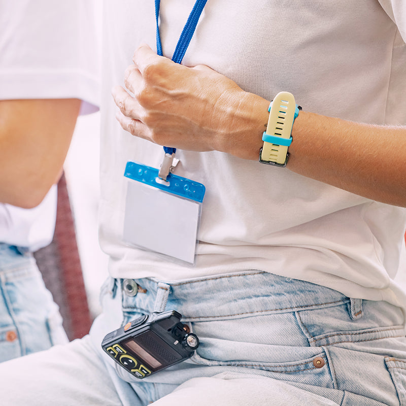 Person wearing a white shirt, blue jeans, and a watch with a lanyard and badge holder.